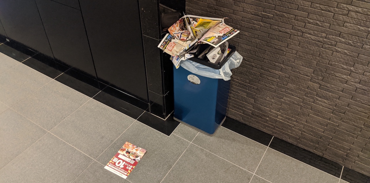 Rubbish bin near mailbox overflowing with junk mail received by residents